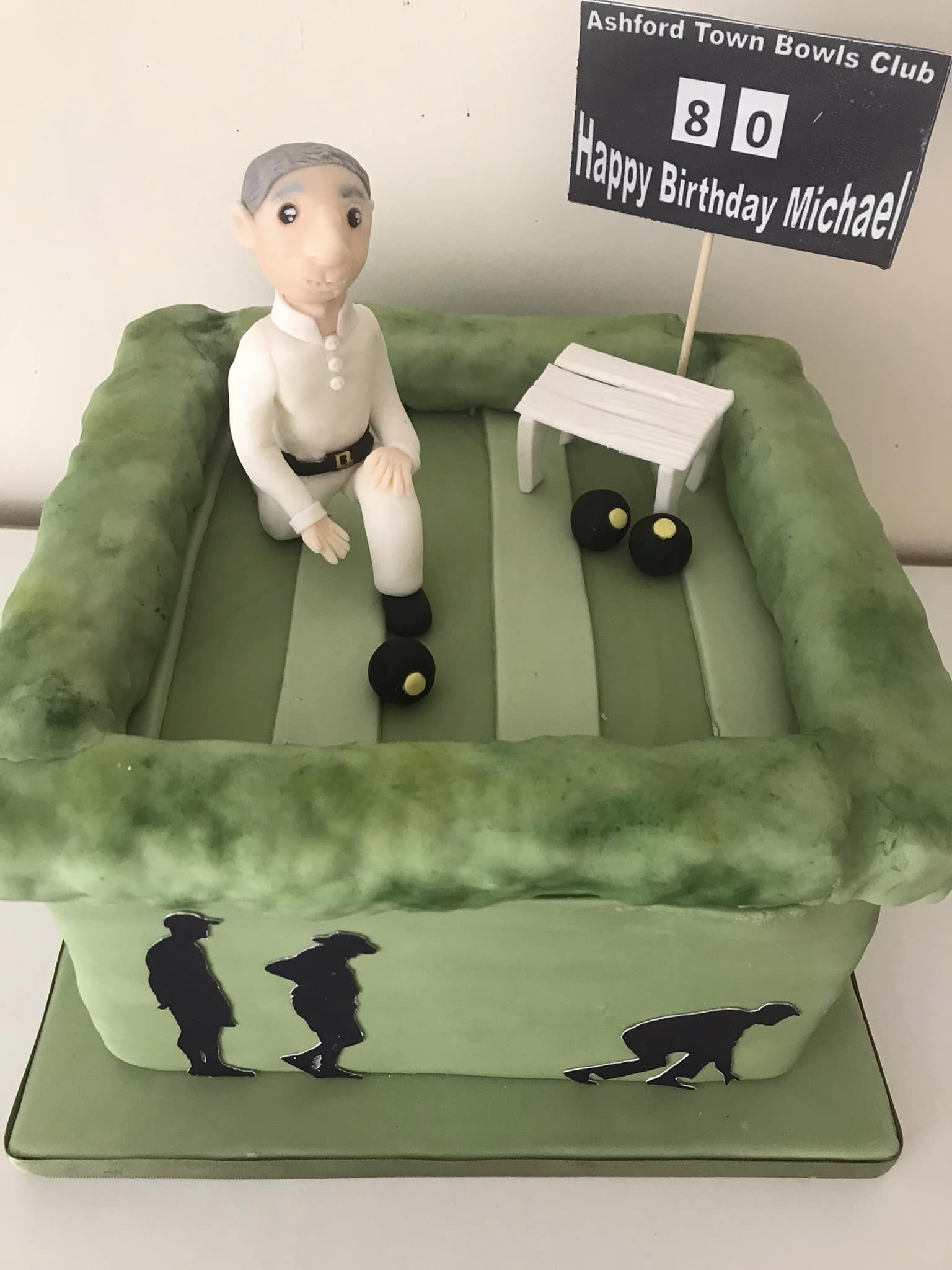cake sculptures of a man on a ashford town bowls club green wearing white and kneeling