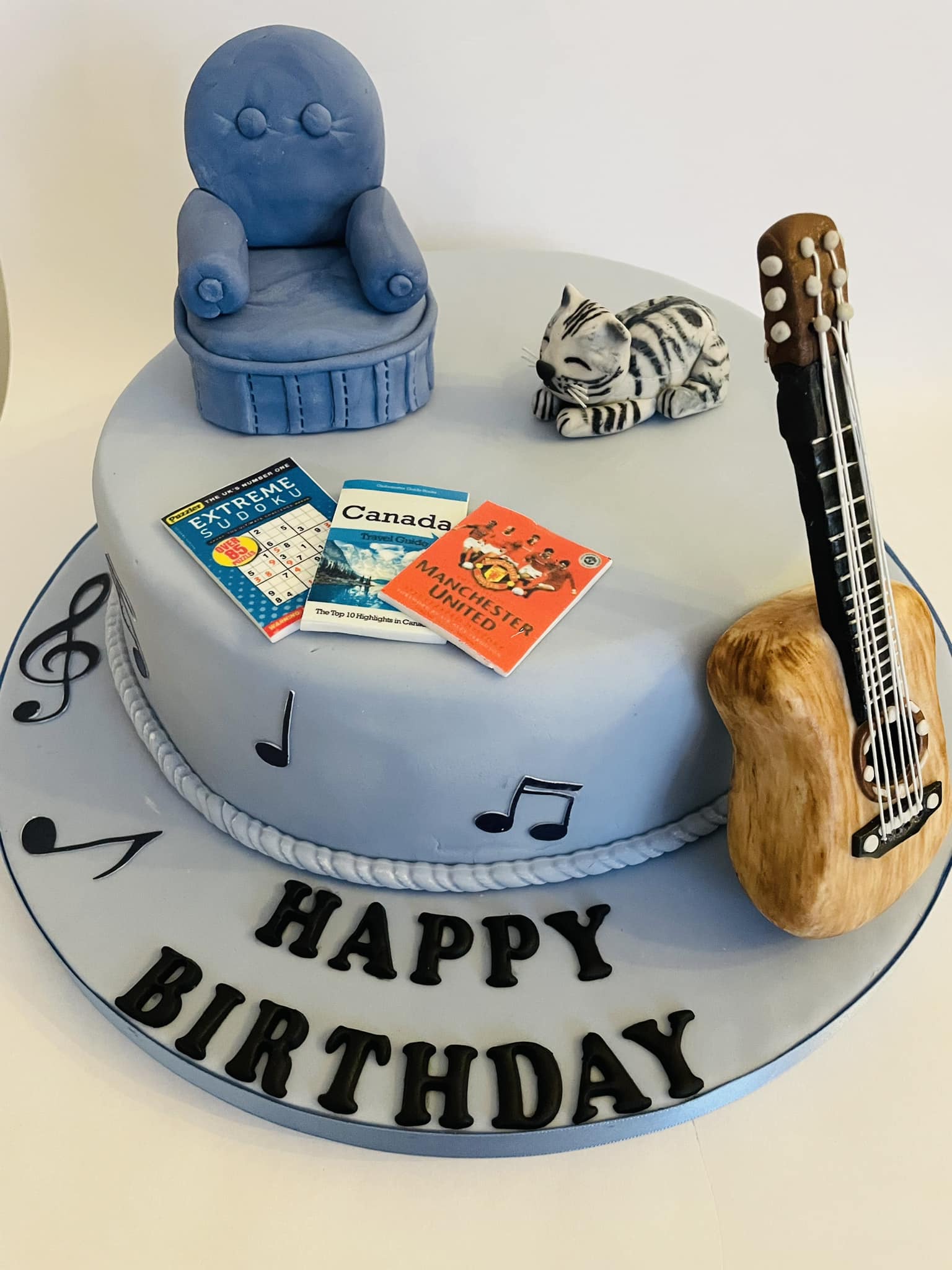 birthday cake featuring a sofa and a cat there is a guitar made of icing at the side